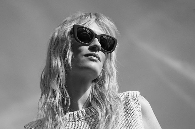 Foto van een vrouw met licht haar die een trendy zonnebril draagt, met de lucht op de achtergrond. De zonnebril benadrukt de nieuwste trends voor 2025. De vrouw kijkt naar voren, haar gezicht is van opzij te zien.