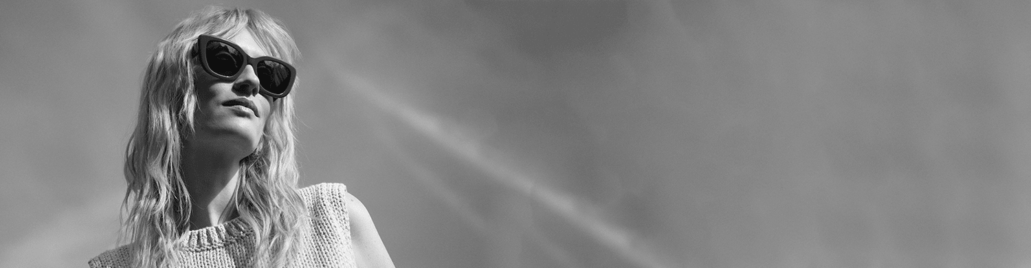 Foto van een vrouw met licht haar die een trendy zonnebril draagt, met de lucht op de achtergrond. De zonnebril benadrukt de nieuwste trends voor 2025. De vrouw kijkt naar voren, haar gezicht is van opzij te zien.