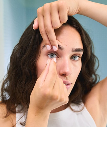 Een vrouw zet een contactlens in haar oog terwijl ze in de spiegel kijkt in een lichte badkamer.